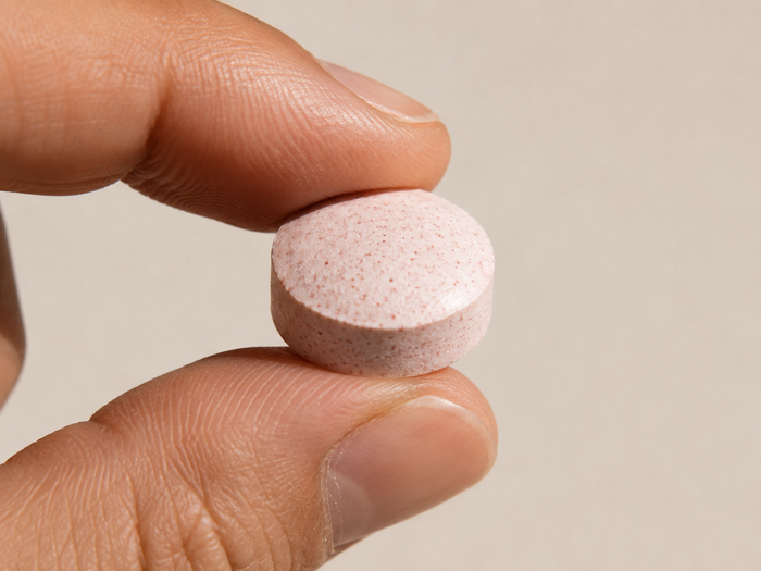 A single blush-pink tablet held between finger and thumb