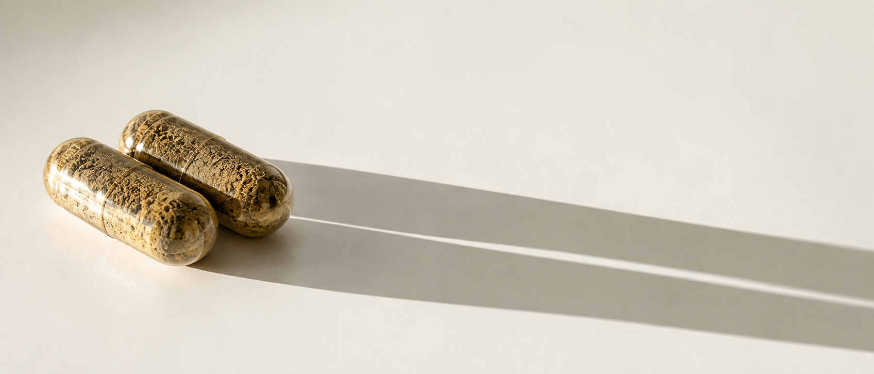 Two veggie capsules throwing long shadows across a pale surface
